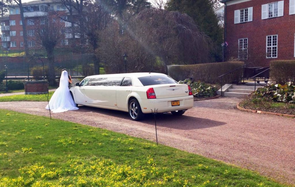 Brudpar med ryggen mot kameran, stående bredvid en vit Chrysler limousine som hyrts in till deras bröllop